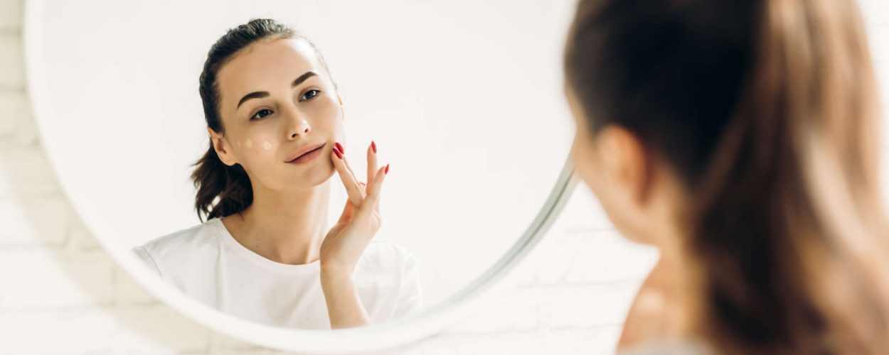 The woman is making up in the bathroom. Woman in bathroom applying cream on face.